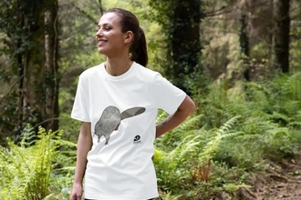 A woman in a woods wearing a white tshirt with an illustration of a beaver on it