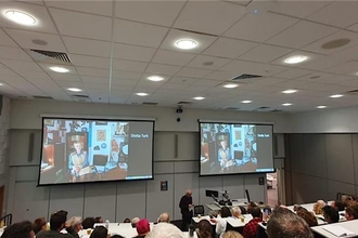 A lecture hall, photo taken from the back of the room. Two huge projector screens on the wall