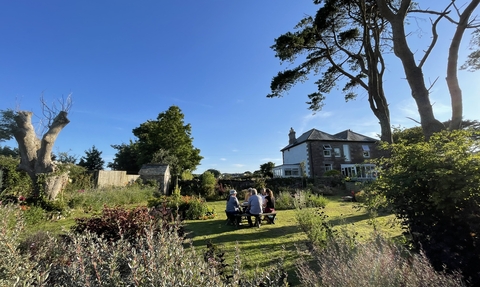 A sunny photograph of Meadowside farmhouse and garden, featuring a variety of shrubs and trees.