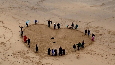 People on a beach arranged in a heart, with text reading Love Your Beach Spread love, not litter