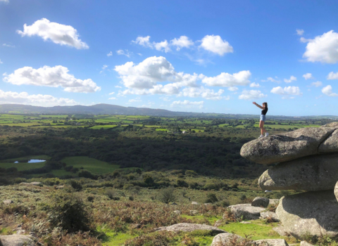 A women stands at the top of Helman Tor with her arms in the air